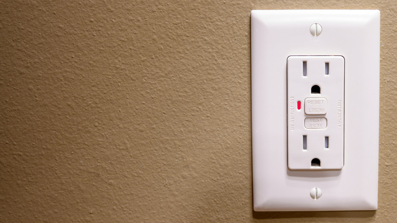 A white GFCI outlet on a brown wall with a red light