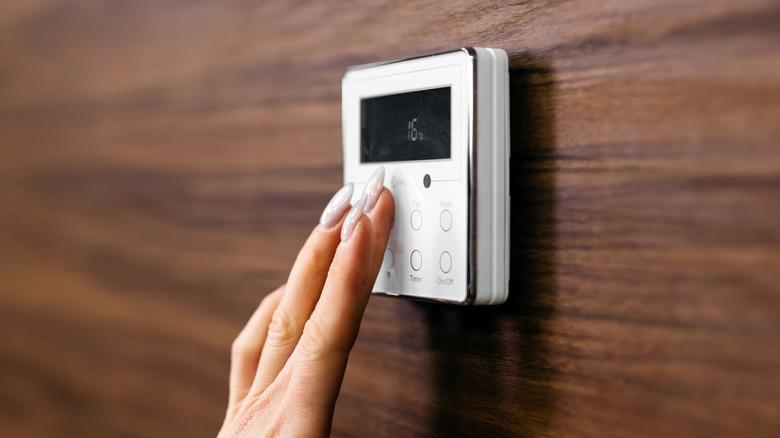 A person with manicured nails pressing buttons on a digital thermostat