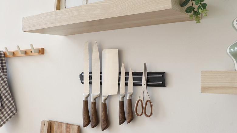Knives stored on a magnetic strip on a kitchen wall.