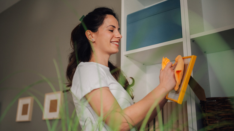 young woman dusting a picture frame with a folded up piece of orange cloth