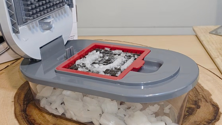 A manual food chopper with onions loaded into the cutting area and diced onions in the tupperware below