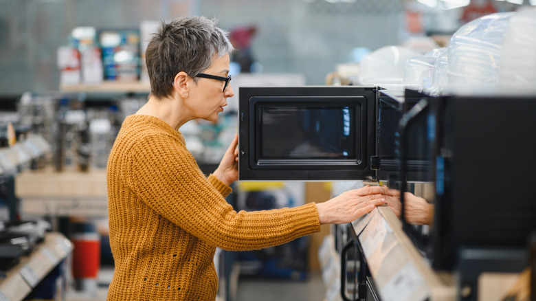 A person inspects a microwave in an appliance store