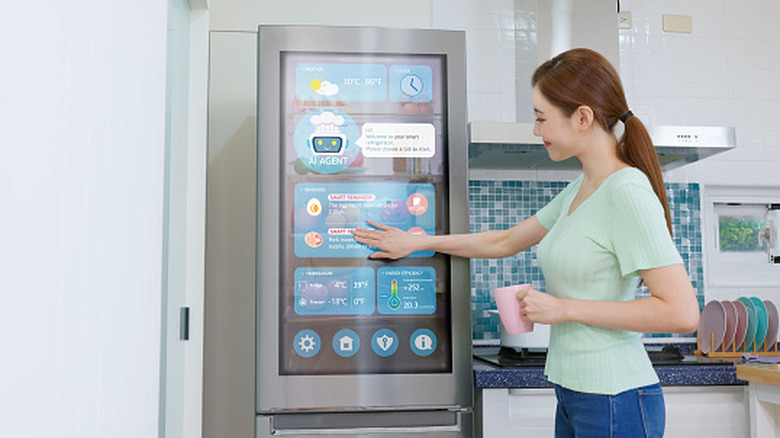 A woman in a green shirt pressing buttons on a smart refrigerator