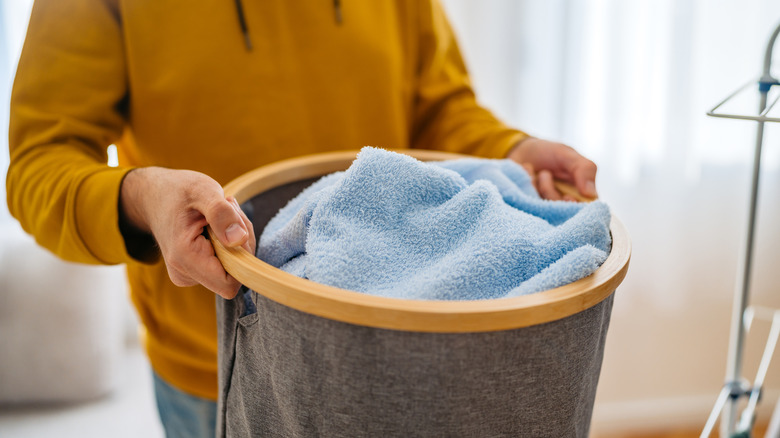 A person carrying a fabric laundry hamper with blue items in it.