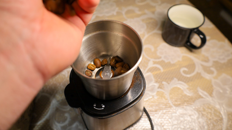A person's hand adding coffee beans to grinder