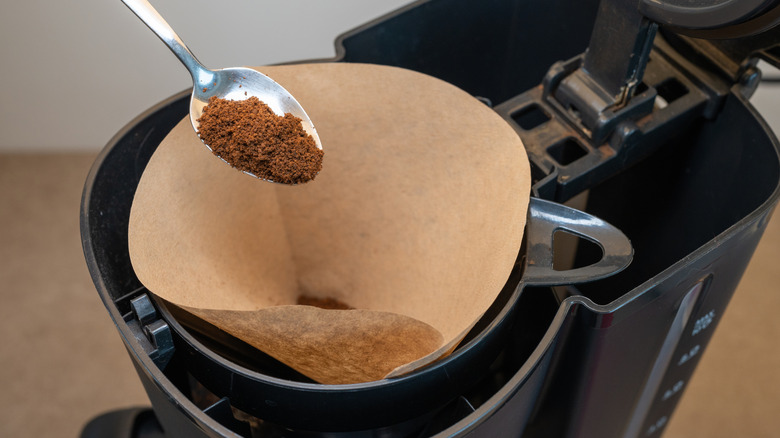 Ground coffee in a spoon above a filter in a coffee machine