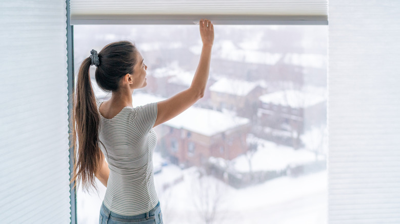 Young girl looks out a window with blinds.