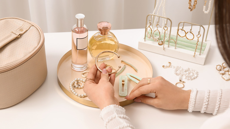 A person looking over their jewelry placed on a tray and a standing rack