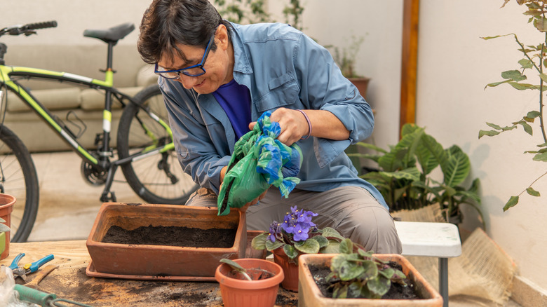 A man pours soil from a bag into a rectangle plastic planter in his patio.