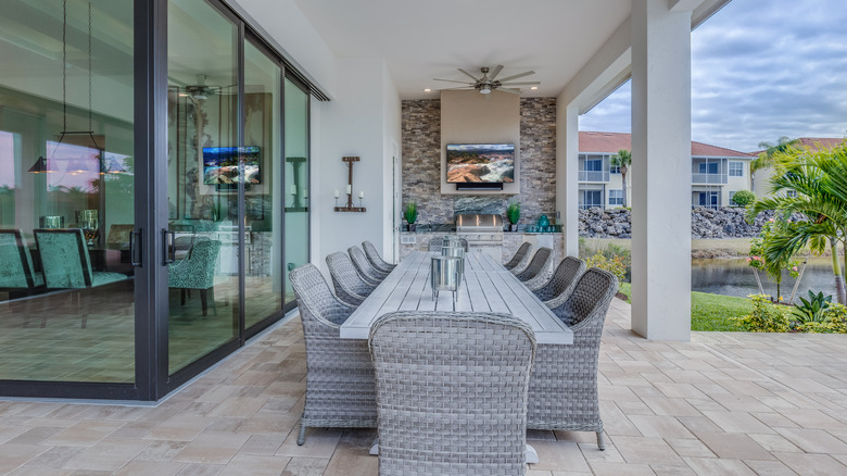 An outdoor TV on a wall above a grill with an outdoor dining table in front of it