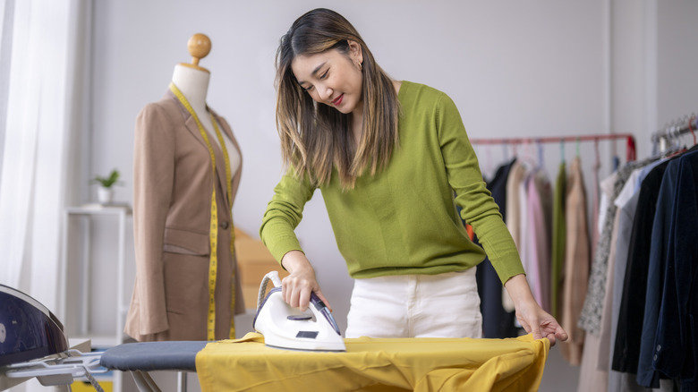 A woman using an iron on a yellow jacket