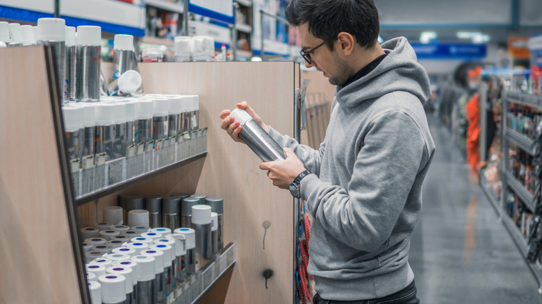 A man holds a can of spray paint while shopping for spray paint at a store