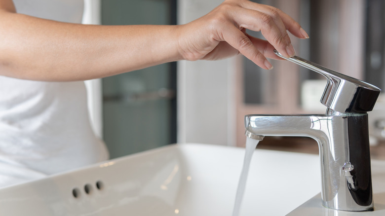 A person turns on a chrome sink faucet