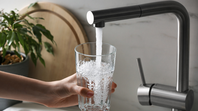 A person fills a glass cup with water from a faucet