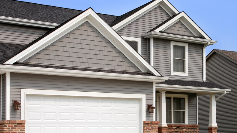 Two-story home with gray vinyl siding and white trim, a white garage door and brick accents also visible