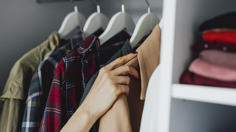 A person's hand sorts through shirts hanging in a closet.