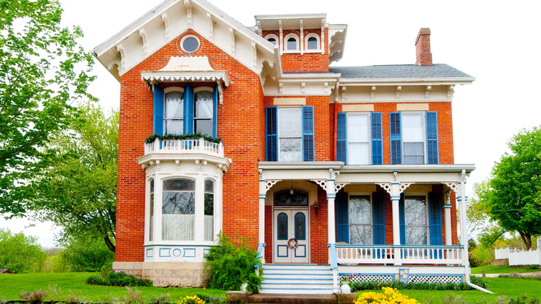 Exterior of old, red brick victorian home with blue shutters and trees nearby