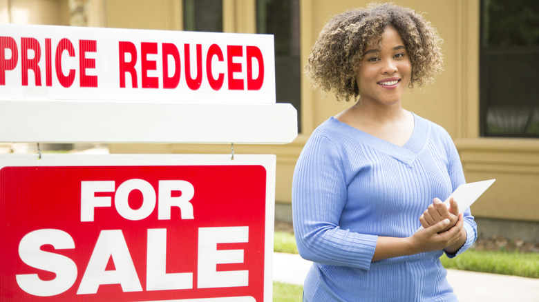 Woman standing next to price reduced for sale sign