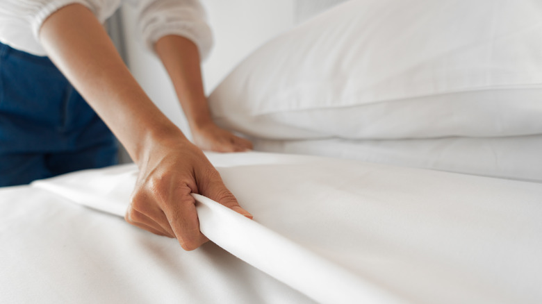 woman's hands pulling white sheets on bed