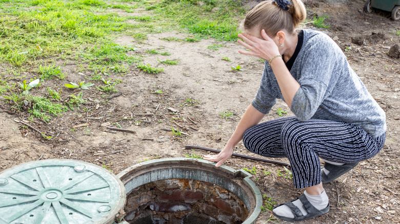 A woman assessing a septic tank with the lid lying on the ground nearby