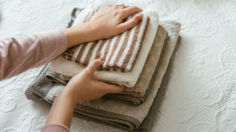Woman with stack of folded, mismatched towels on bed