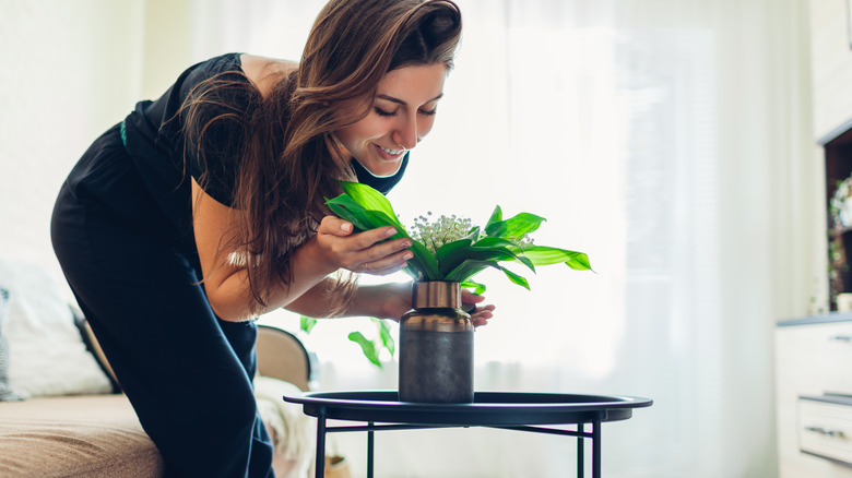 woman admiring lily of valley in a vase in a living room