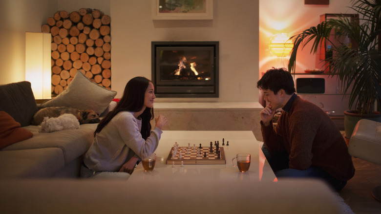 Man and woman playing chess on coffee table.