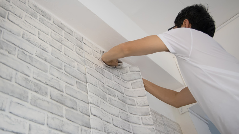 man putting up faux brick wallpaper 