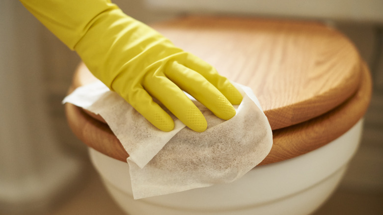 Person wiping wood toilet seat with disinfecting wipe