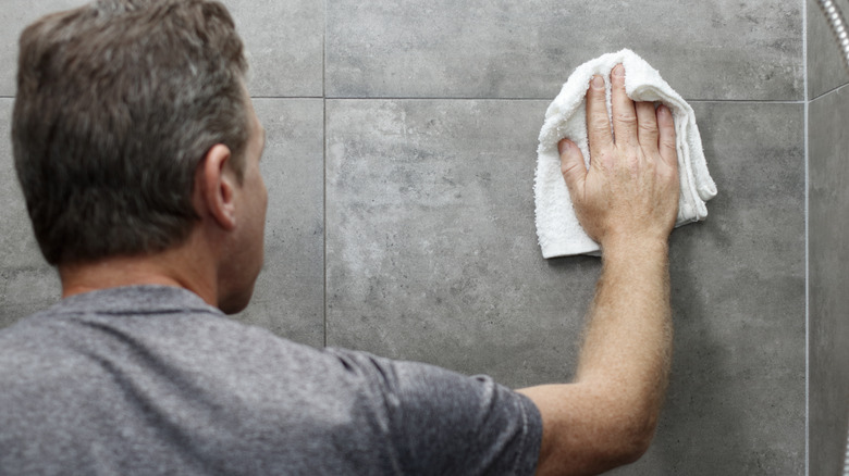 man cleaning stone shower with a white washcloth