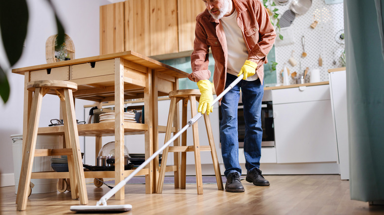 A man cleaning the kitchen floor with an extra long mop