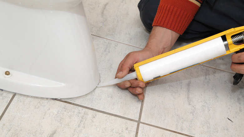 person applying caulk around toilet