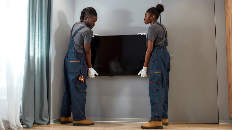 Two people mounting TV on gray wall in home