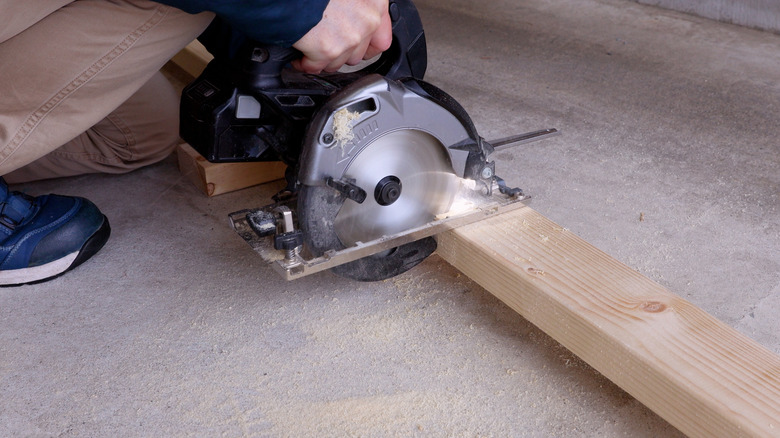 A person uses a circular saw to cut a 2x4