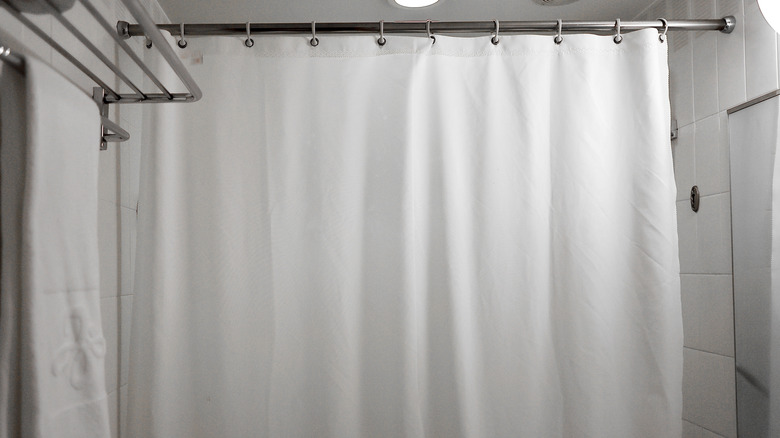 A clean, modern bathroom with a white shower curtain liner handing.