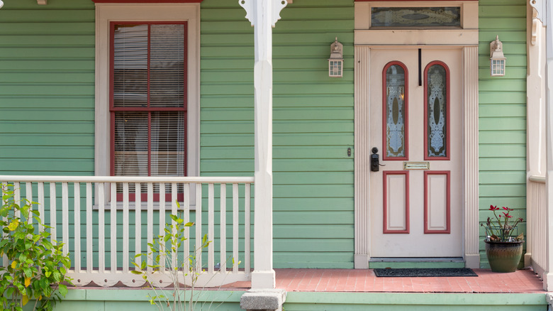 The porch of a green-paneled house with a white and red door