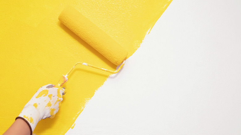Yellow roller brush painting a white wall 
