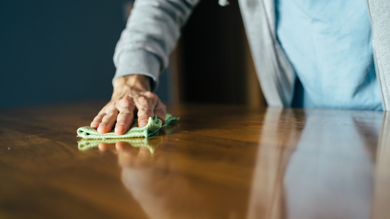 A person cleaning a wooden table with a cloth