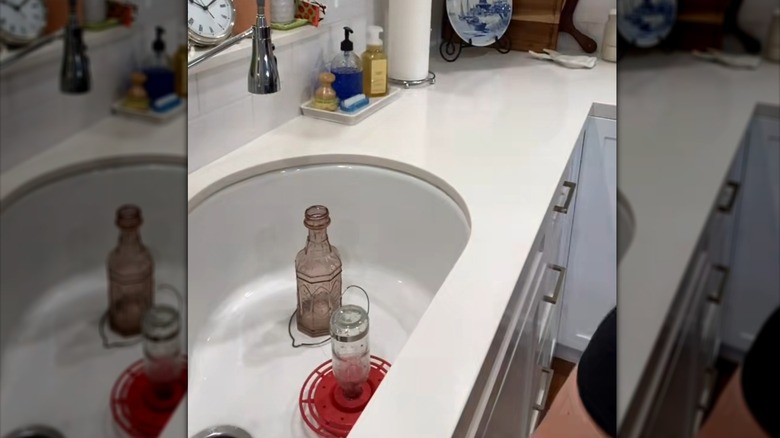 Woman washing two hummingbird feeders well with water in her sink