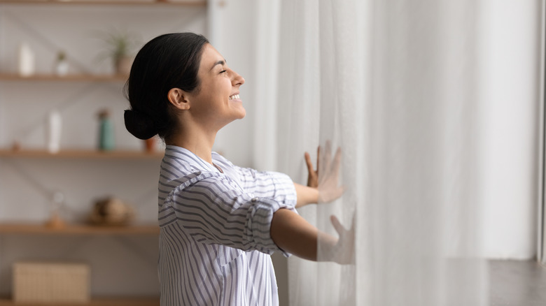 Woman smiling, holding curtains open
