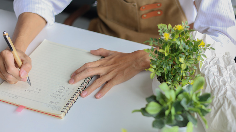 Person making a list of gardening items beside plant pots
