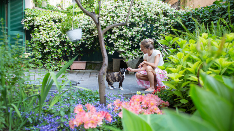 Woman petting a cat in the middle of a flower garden