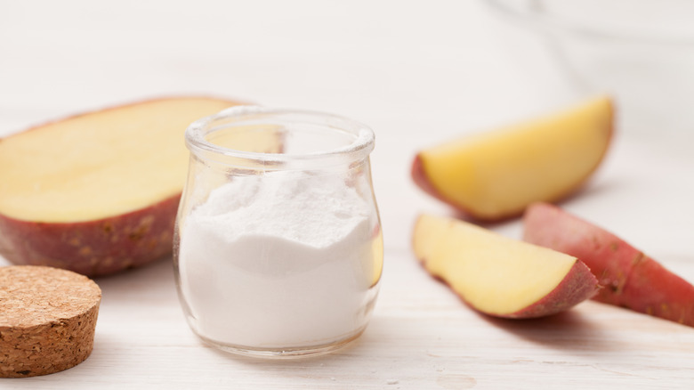 Jar of baking soda and cut potato pieces placed on a wooden surface