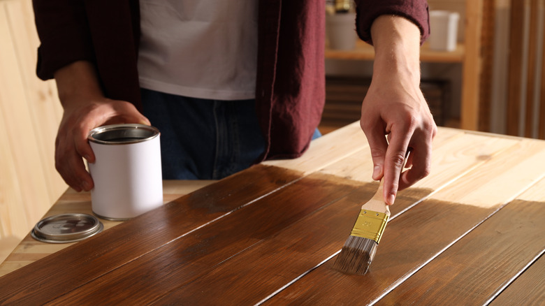 A person applies dark stain to a wood surface
