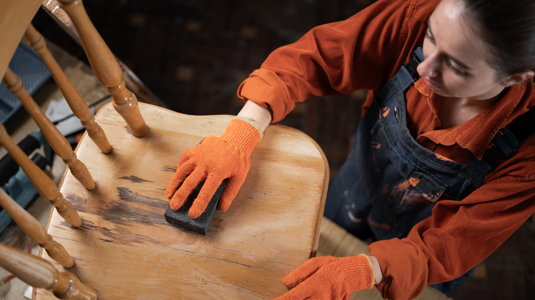 A woman sanding the seat of a wooden chair