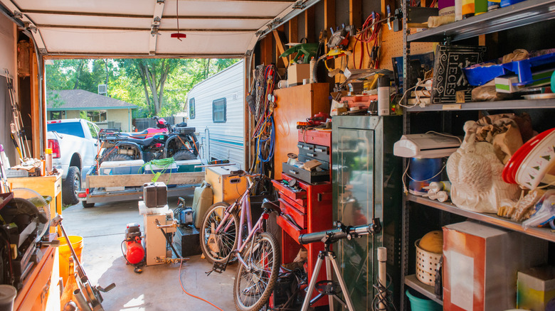 Garage with open door, shelves filled with things, pegboards, and items on the floor.