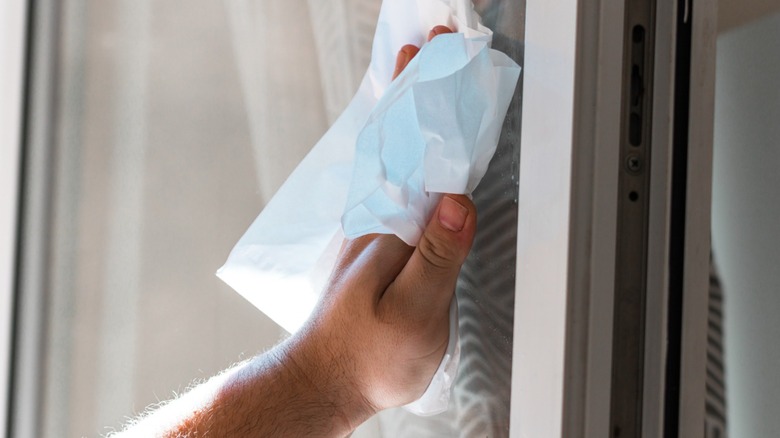 Hand cleaning a glass window with a paper towel.