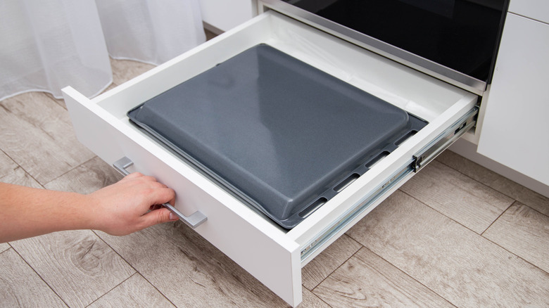 Hand pulling out oven drawer with cookie sheets