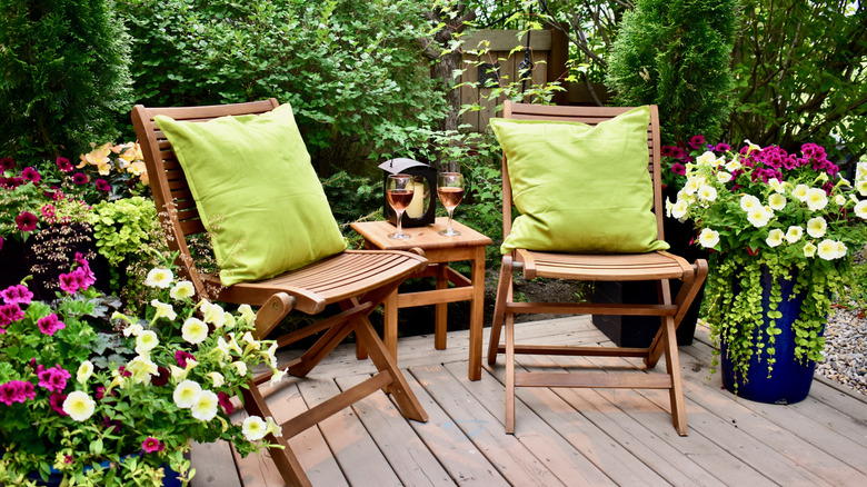Two outdoor furniture chairs, and a small table on a deck, surrounded by plants