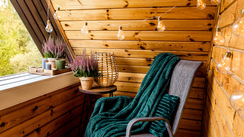 A cozy balcony with wood panels and a chair with an outdoor blanket